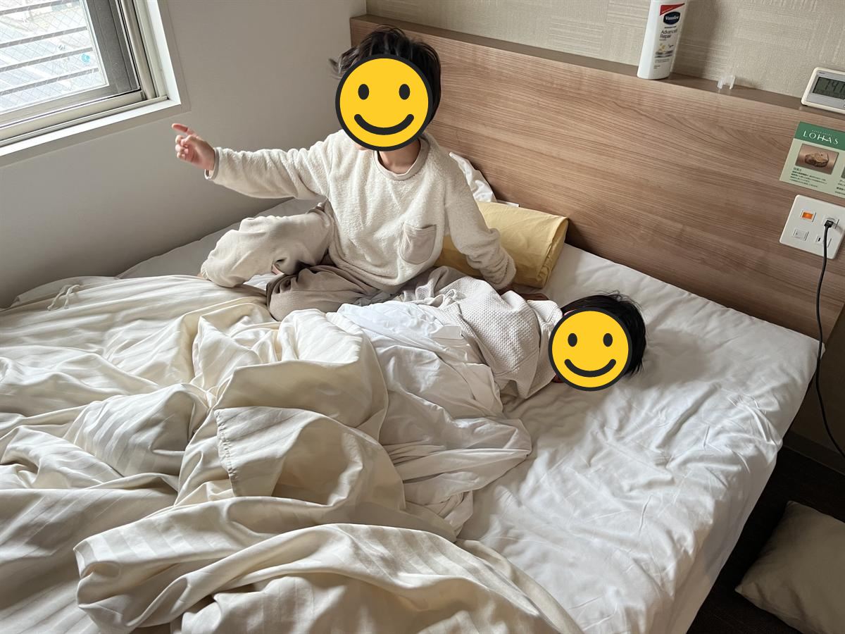 ホテルのベッドで起き上がる小学生と、まだ眠っている小学生