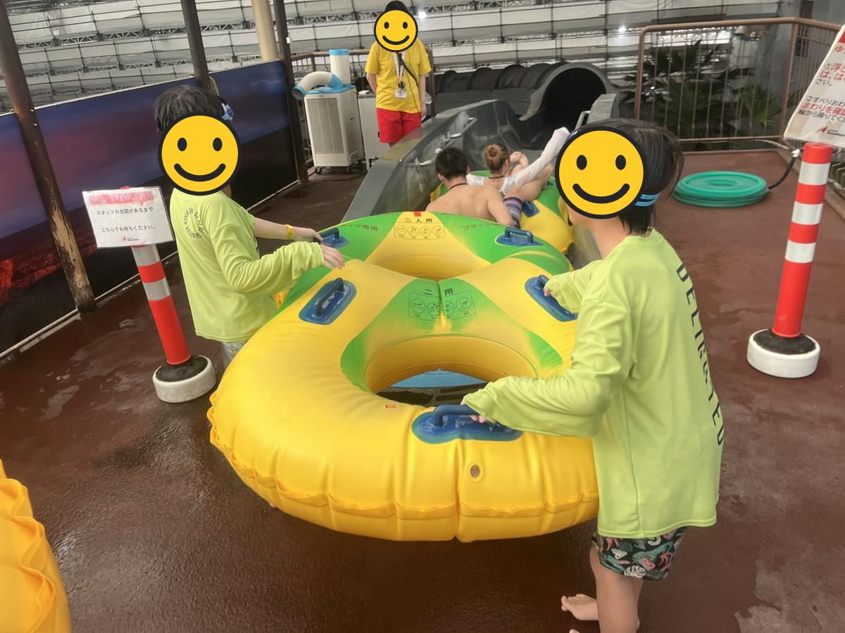 2人用の浮き輪を持ってウォータースライダーの順番を待つ小学生2人