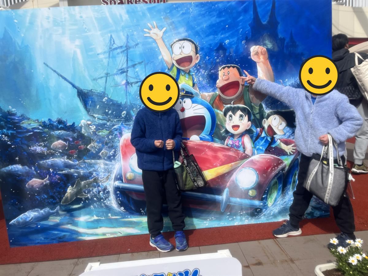 スパリゾートハワイアンズのドラえもんコラボ看板前で記念撮影する小学生2人