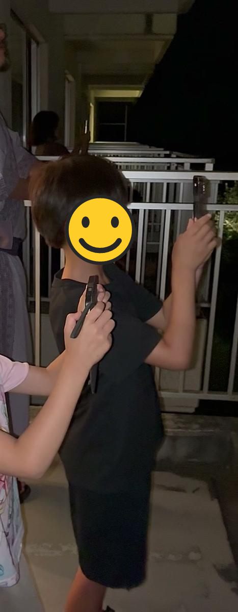 バルコニーでスマホを両手で構えて花火を撮る男の子