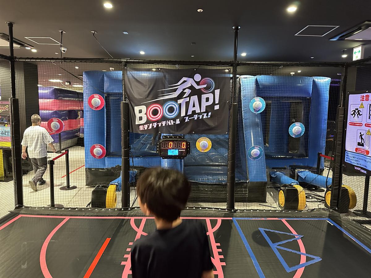 BOOTVERSE多摩のBOOTAP!エリア。ネットで囲まれたコートに、青いエア遊具とタッチ用のボタンが並ぶ