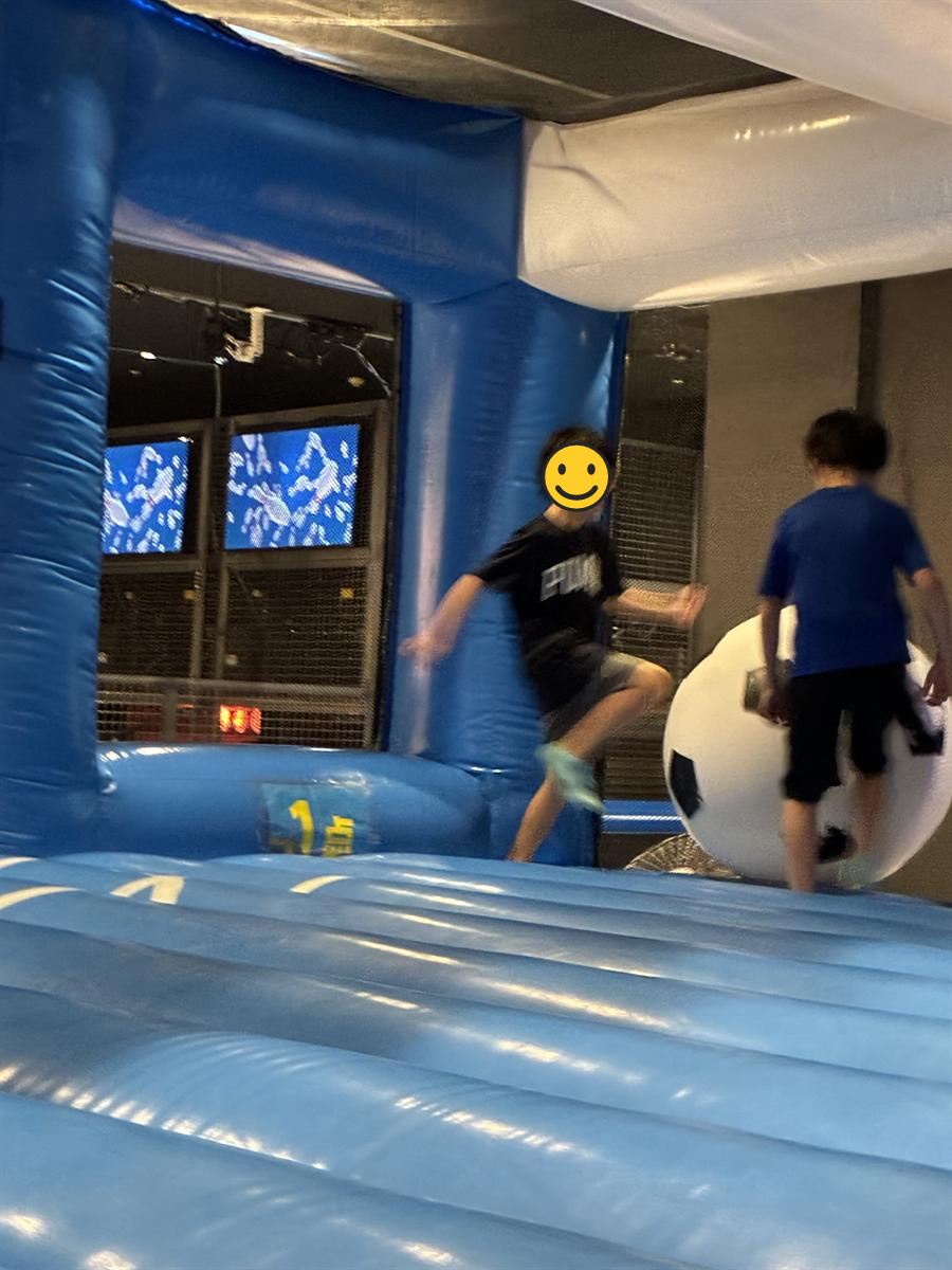ジャンボサッカーで巨大な白黒のボールを追いかける子どもたち。足元は青いエアマット