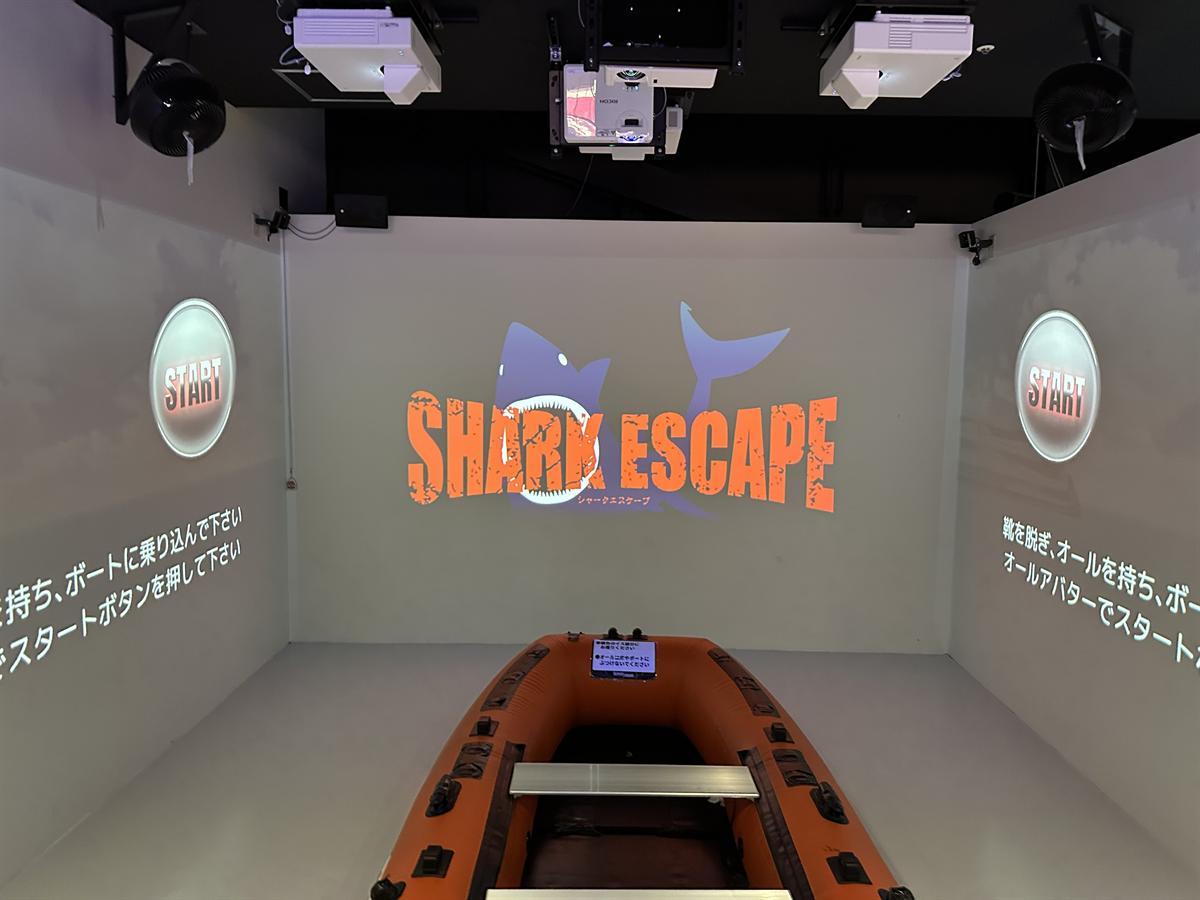 シャークエスケープのボート。プロジェクションマッピングされた壁の前にオレンジ色のゴムボートが置かれている