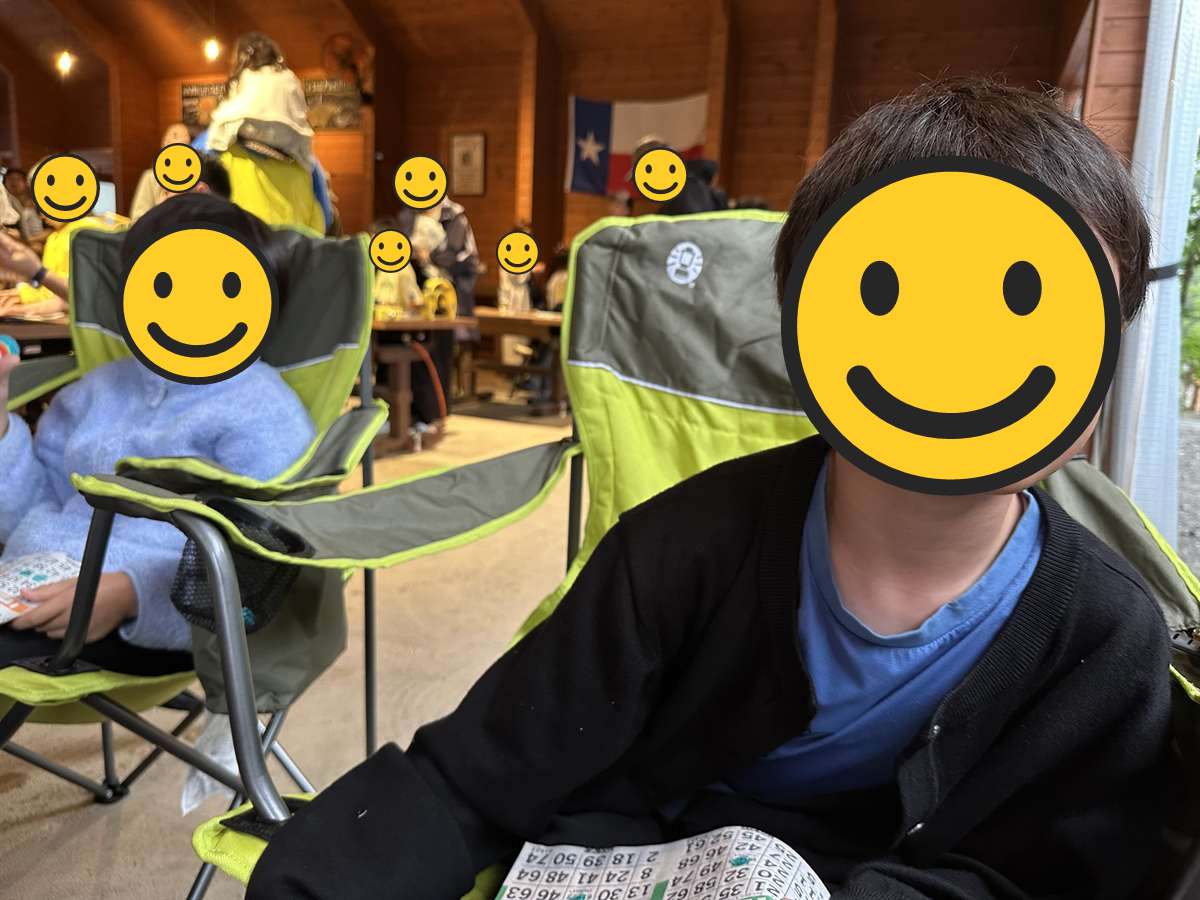 屋根のある会場でビンゴカードを持ってアウトドアチェアに座る子ども2人