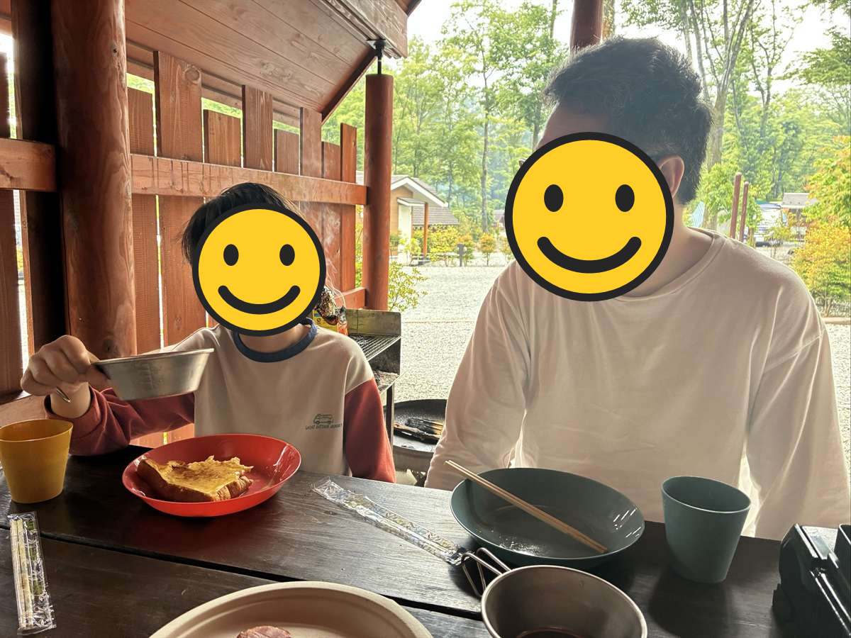 キャビンの前の木のテーブルで朝ごはんを食べる子どもと父親