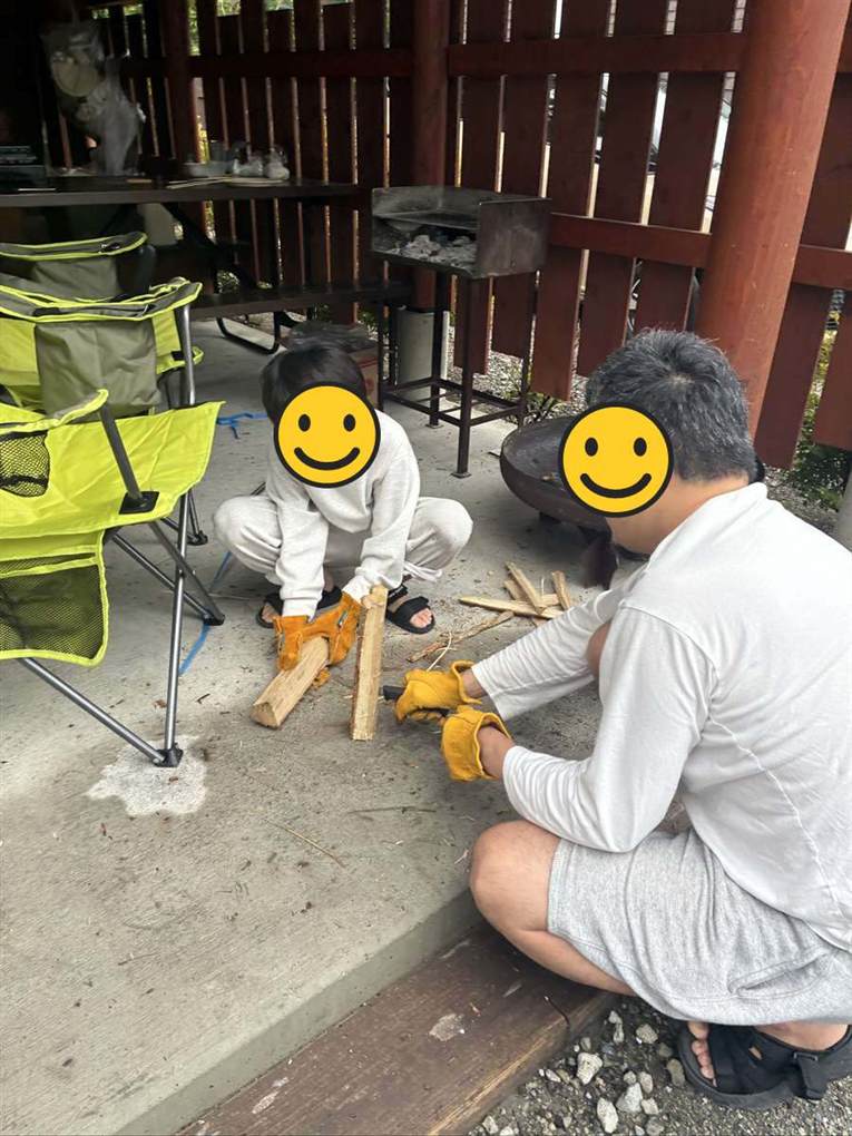 革手袋をして焚き火台の前で薪を並べる子どもと大人