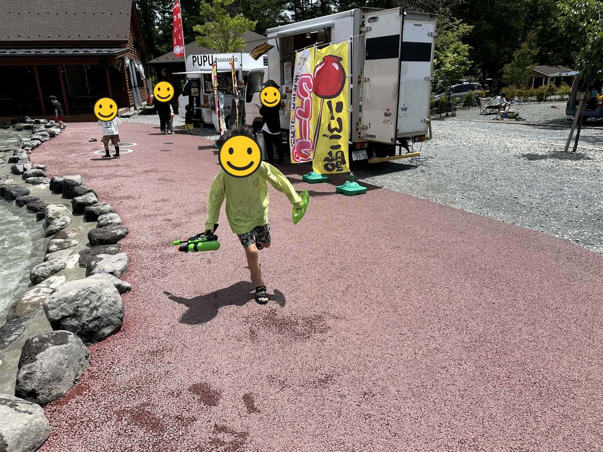 浅い人工の水路のそばを水鉄砲を持って走る子ども
