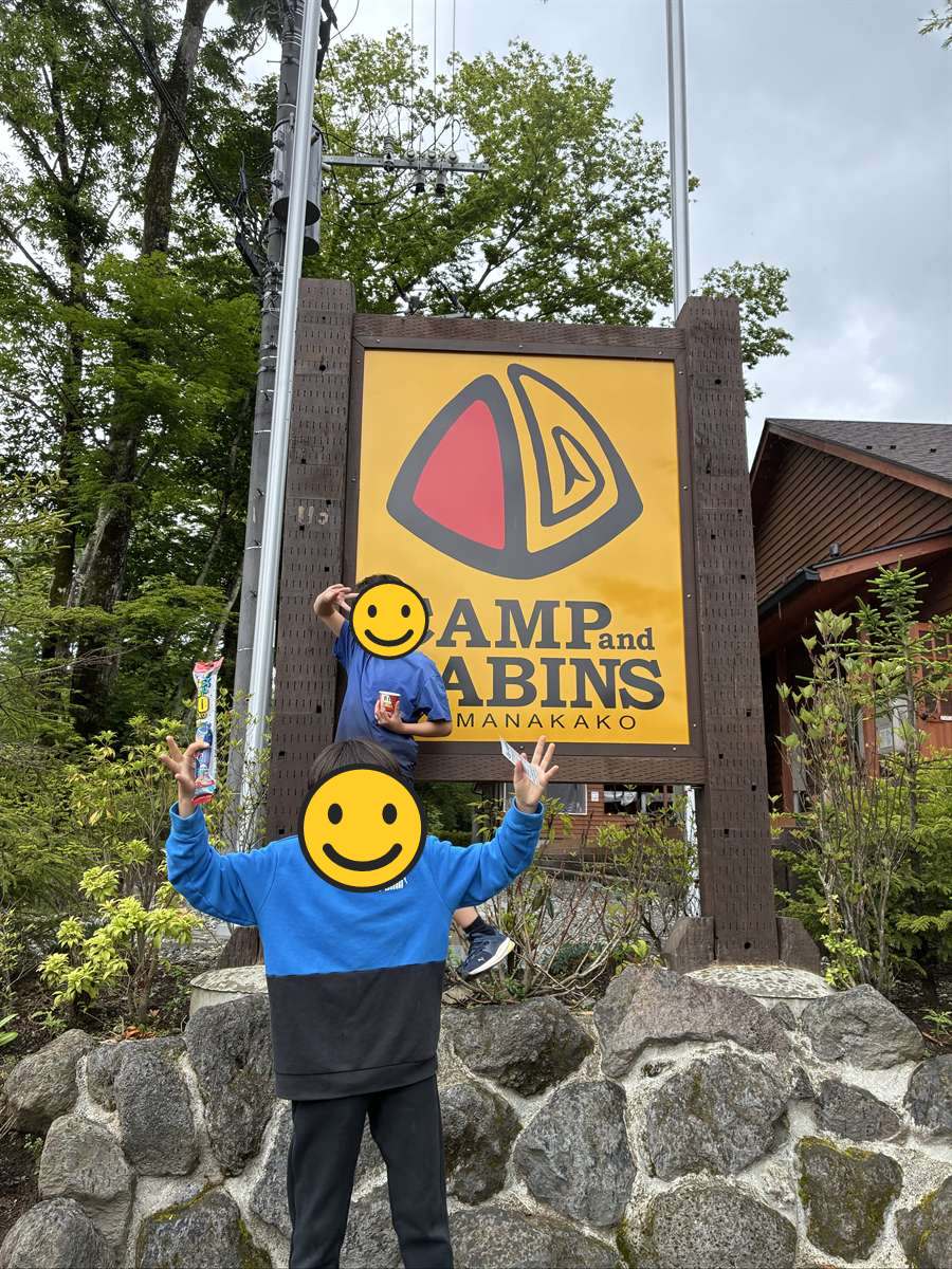 キャンプアンドキャビンズ山中湖の看板の前でポーズをとる子ども2人