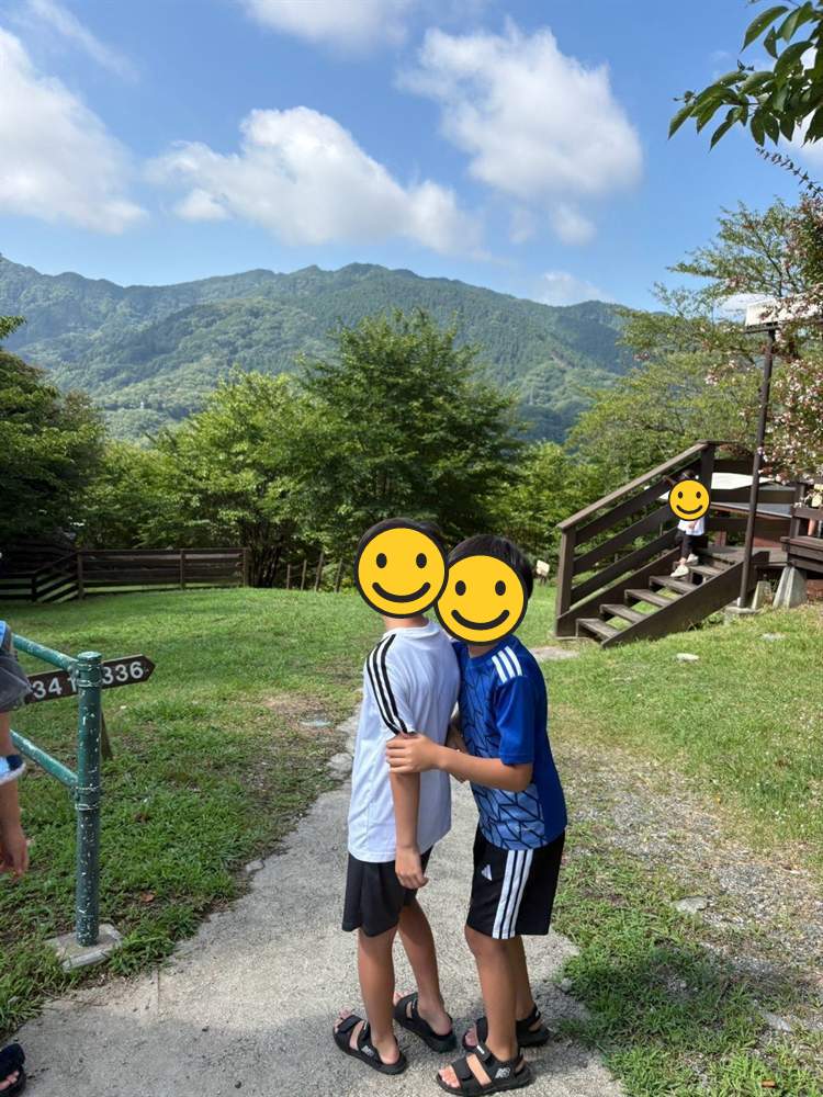 コテージの前で肩を組む兄弟と、奥に見える山