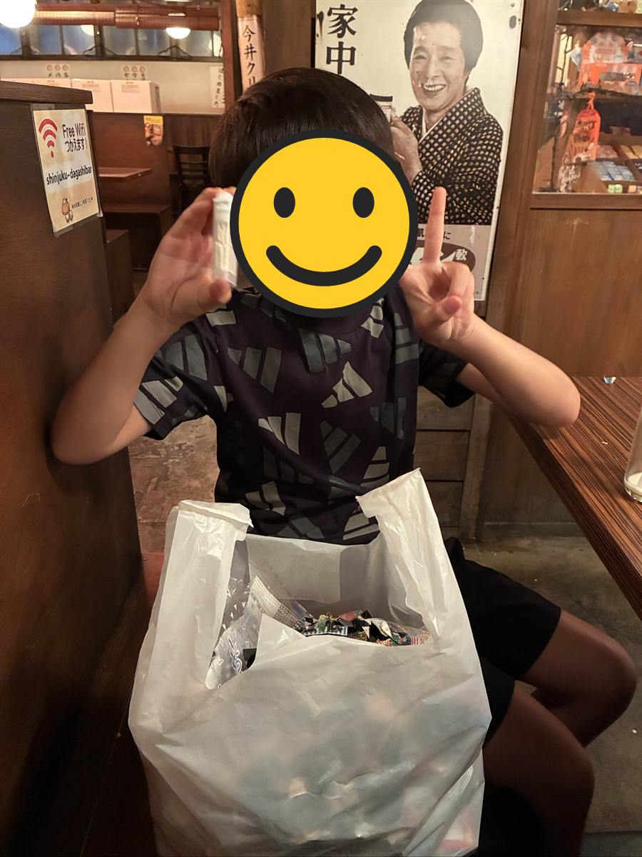 食べ終えた駄菓子の袋でいっぱいのレジ袋を抱えてピースする長男
