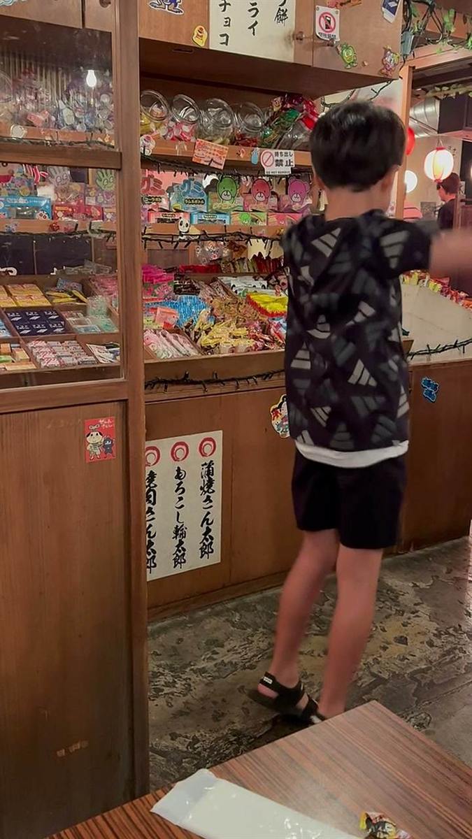 駄菓子がびっしり並んだガラスケースの前で物色する子どもの後ろ姿