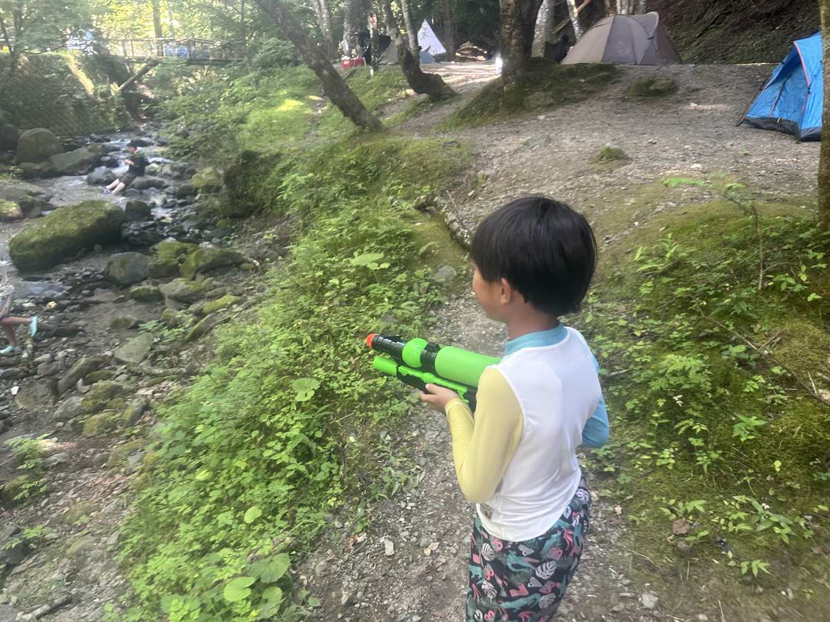 岩がごろごろした沢に向かって水鉄砲を構える子どもの後ろ姿