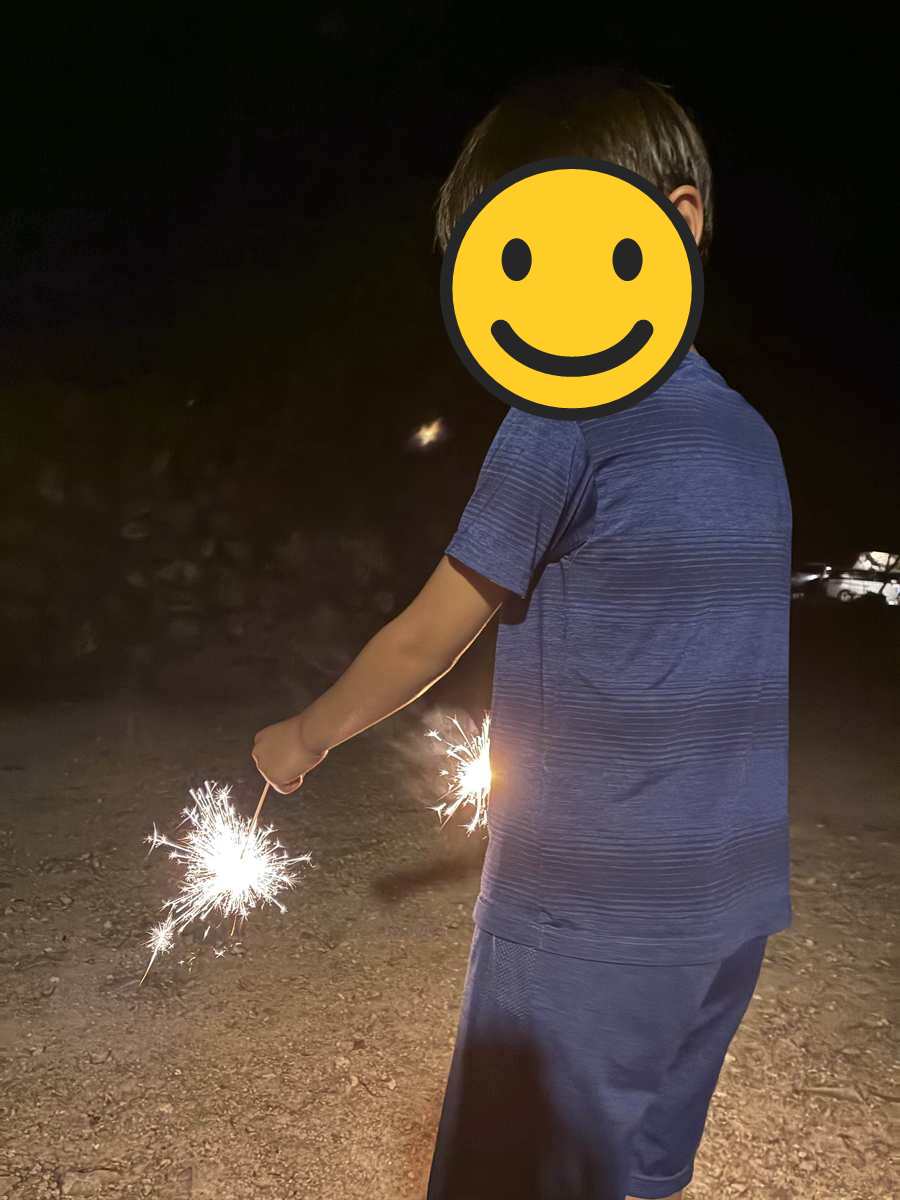 暗いキャンプ場で手持ち花火に火をつけて振り返る子ども