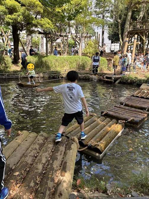 池に浮かぶ丸太のいかだを渡る子どもと、対岸で順番を待つ列