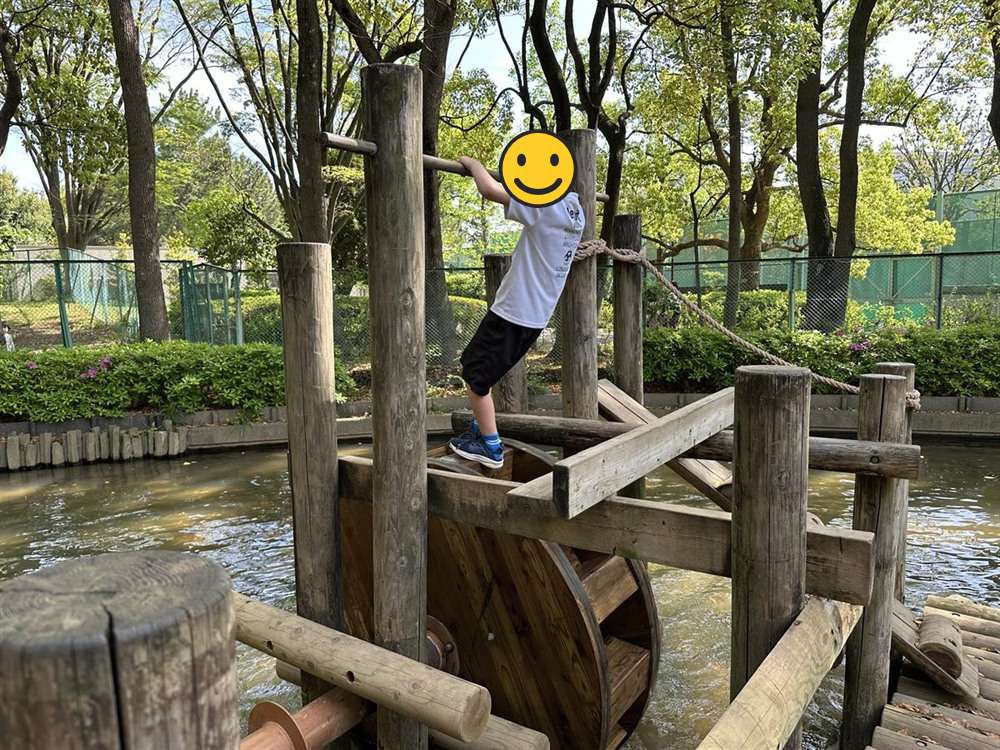 平和の森公園の水上アスレチック、池の上の水車型遊具に挑む子ども