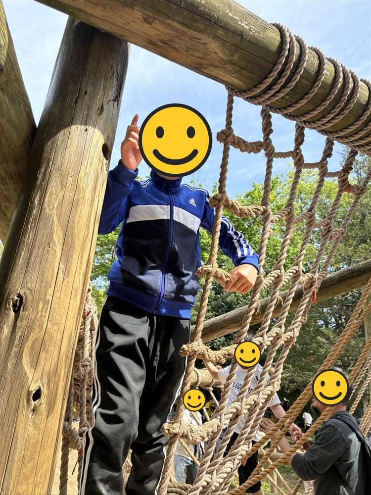 ロープの網の上から次に挑む遊具を指差す子ども