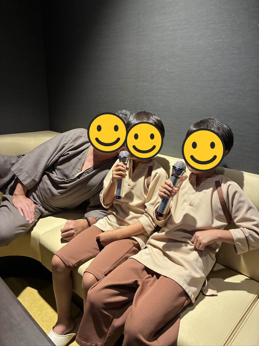 黄色いソファのカラオケルームでマイクを持つ子ども2人とパパ