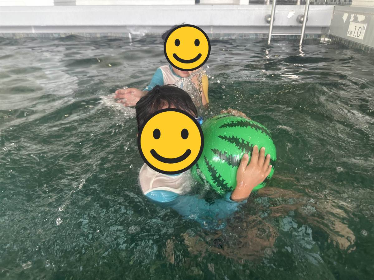 室内プールでスイカ柄のビーチボールを抱える子ども2人