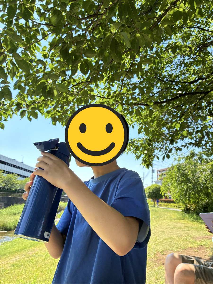 木陰で水筒の麦茶を勢いよく飲む子ども
