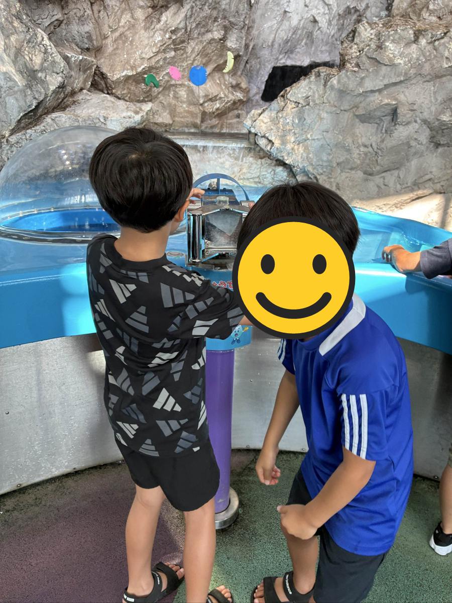 岩場の展示の前でハンドル式の装置を操作する子ども2人