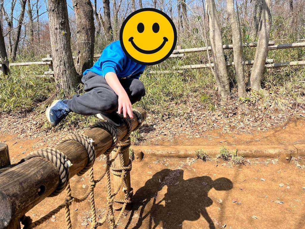 ロープが巻かれた丸太の上を飛び越えようとしている子ども