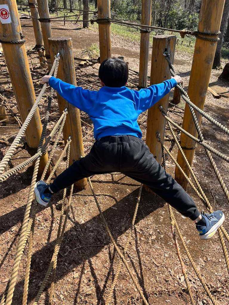 ロープが張られた丸太の遊具に、手足を大きく広げて張りついている子ども