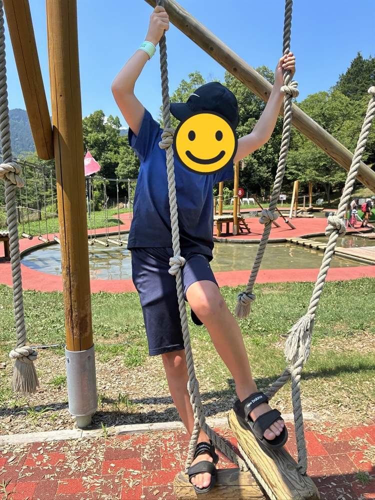 ロープにつかまって水の上の丸太を渡る子ども