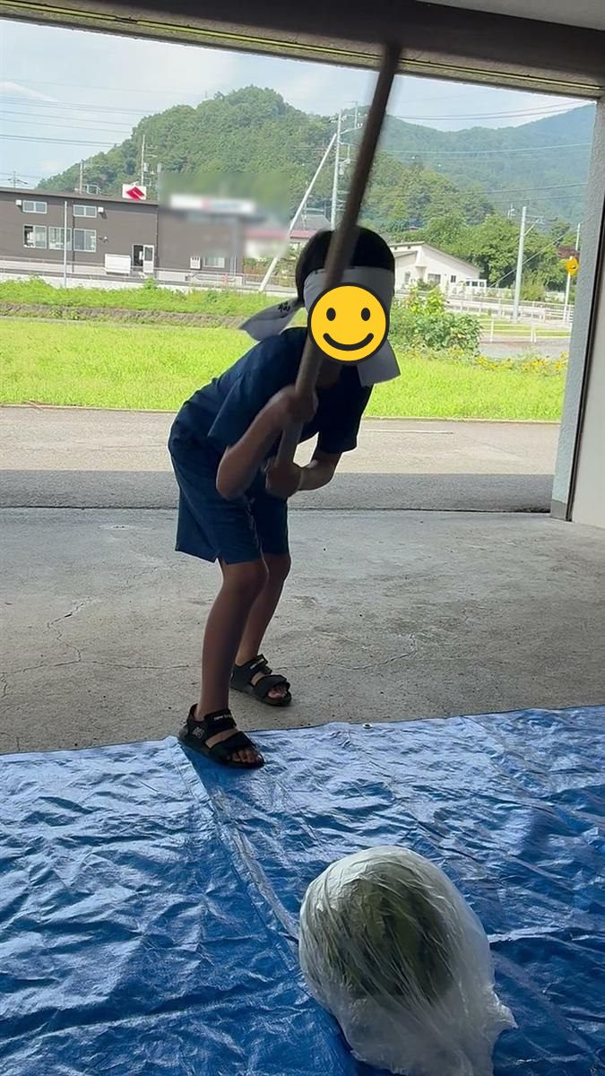 目隠しをして棒を振りかぶる男の子とブルーシートの上のスイカ