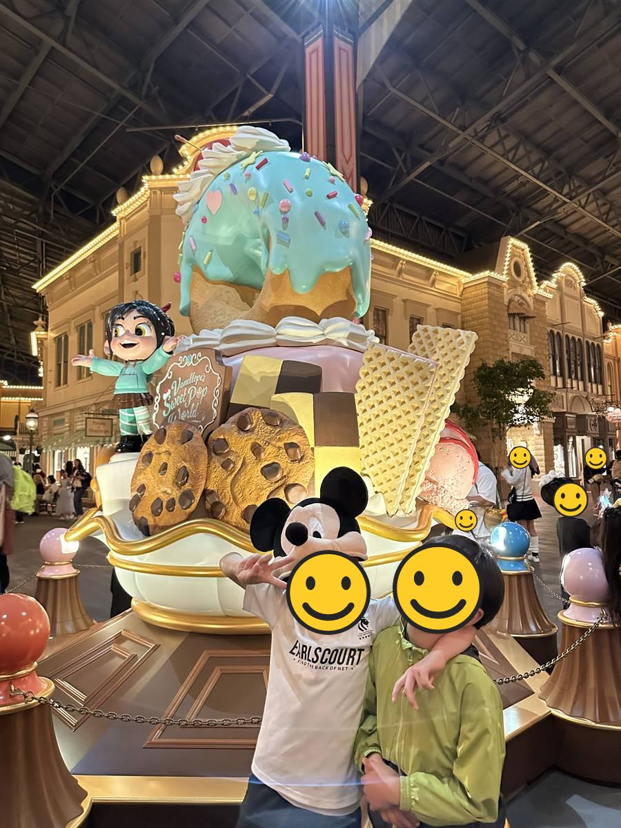 夜のアーケードでお菓子のオブジェの前に立つ子ども2人