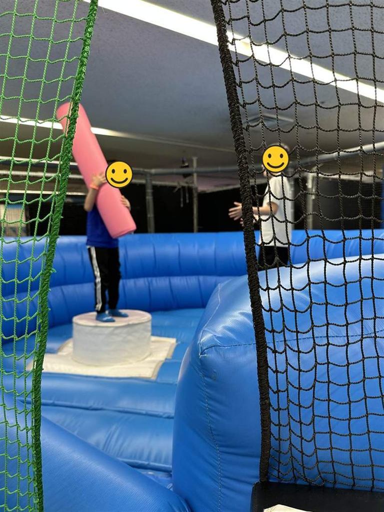 エア遊具の上に立ち、ピンクの筒状クッションを構える子ども。向かい合ってもう1人が立っている