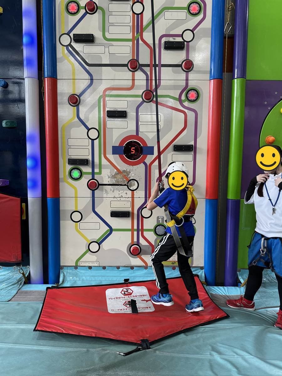 タイマー表示のついた壁を登り始める子ども。右側にスタッフが立って見守っている
