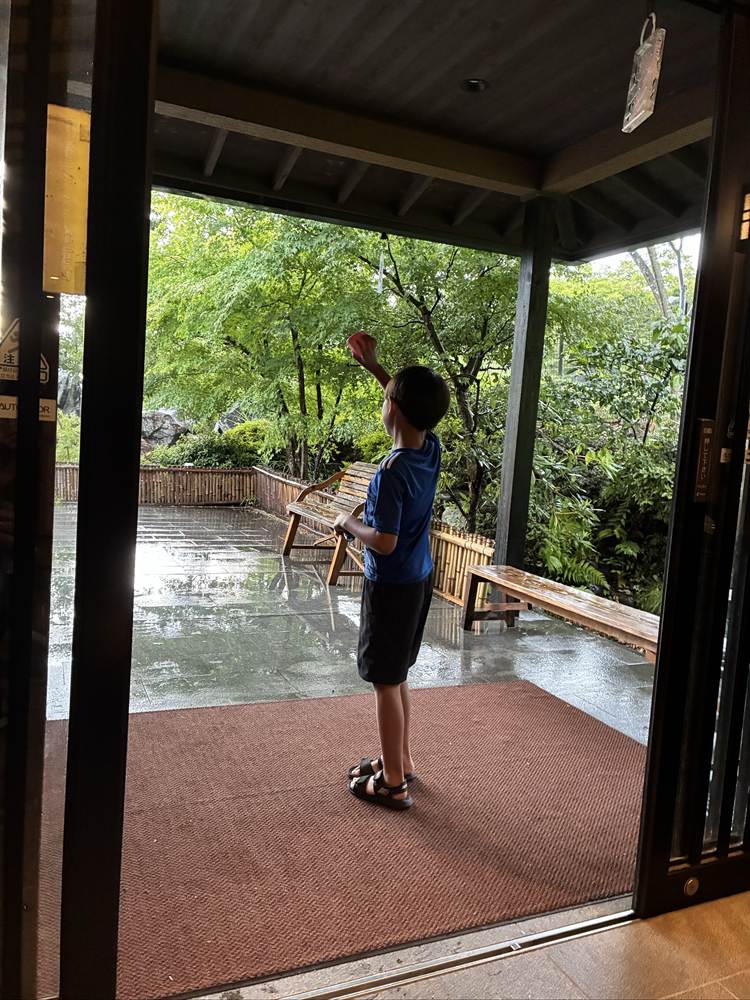 さがみ湖温泉うるりの出入口から雨に濡れた庭を見る子ども