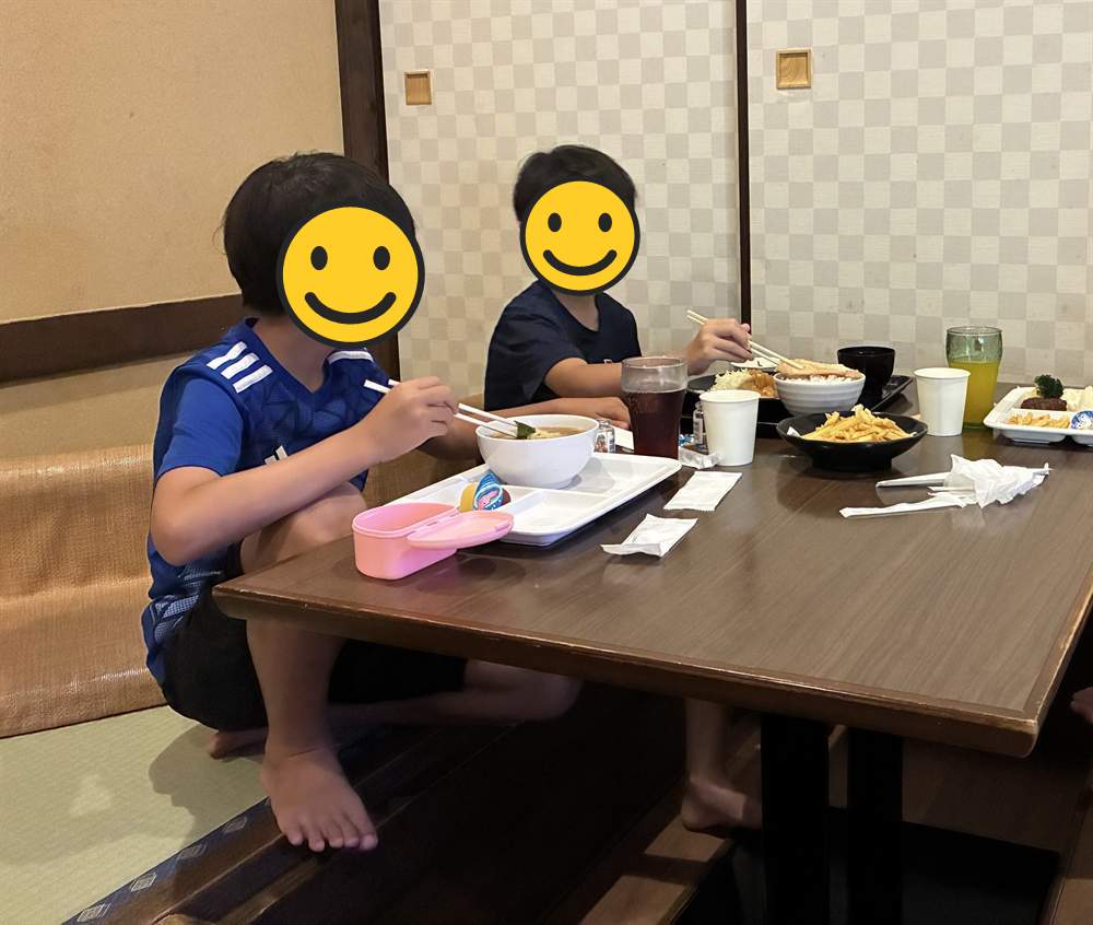 和室の食事スペースでうどんと天ぷらを食べる兄弟