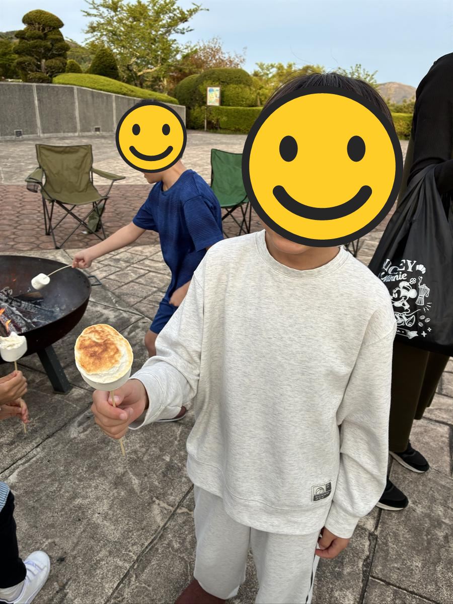 焚き火で焼いたマシュマロを串ごと見せる子ども