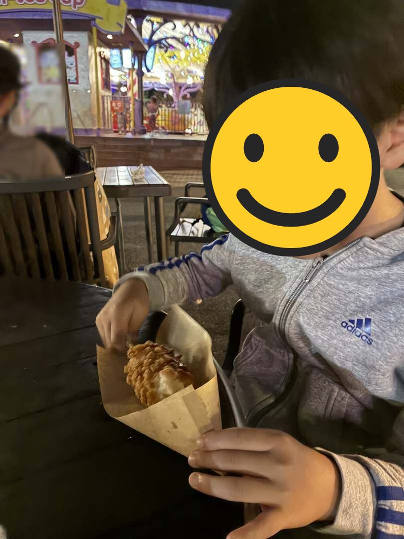 夜の富士急ハイランドのテラス席で、チーズハットグを食べるこども