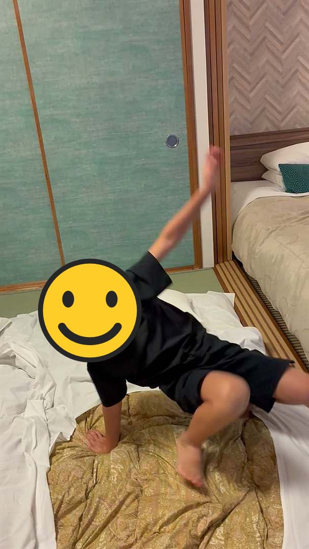 ホテルの和室の布団の上で、側転をするこども。奥にベッドが見える