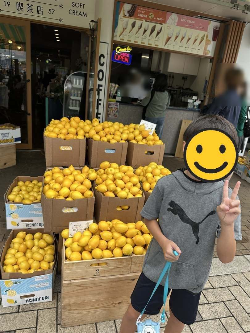 レモンが木箱に山積みになったお店の前でピースする次男