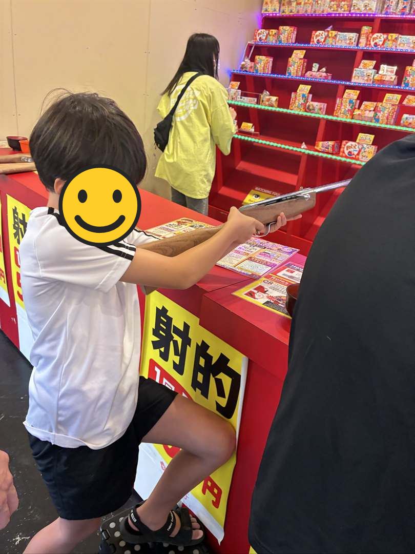 新世界の射的屋で、コルク銃を構えて景品の棚を狙うこども