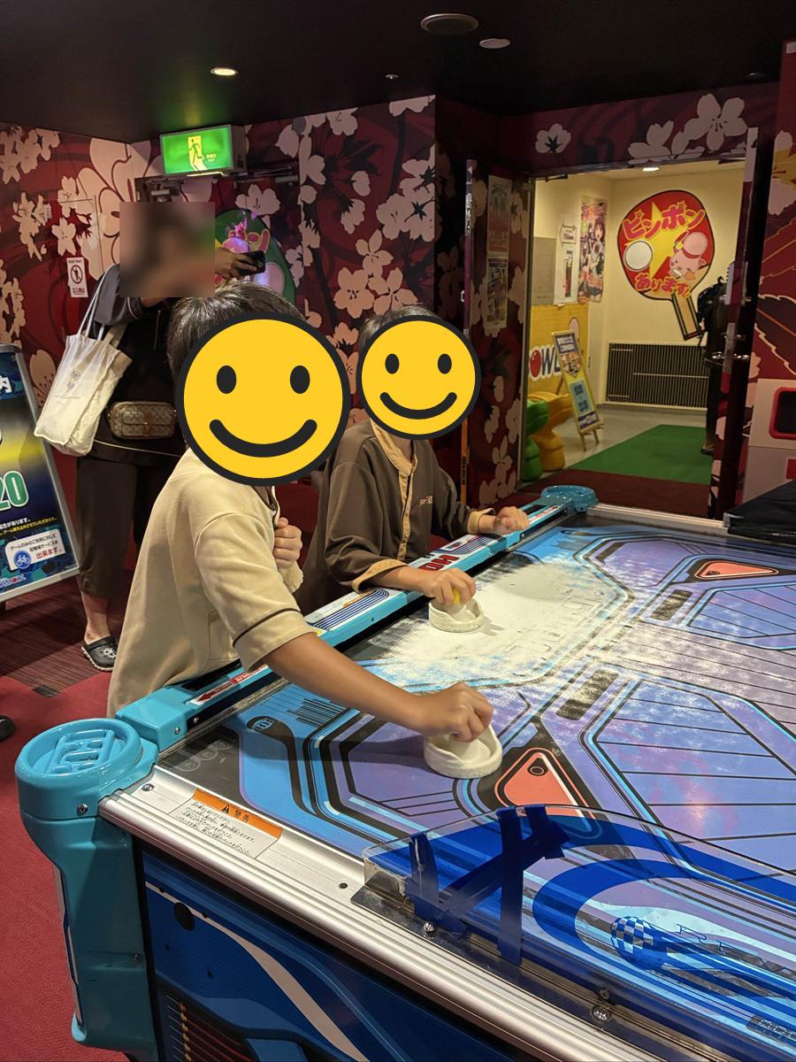 桜柄の壁のゲームコーナーで館内着のままエアホッケーをする子ども2人