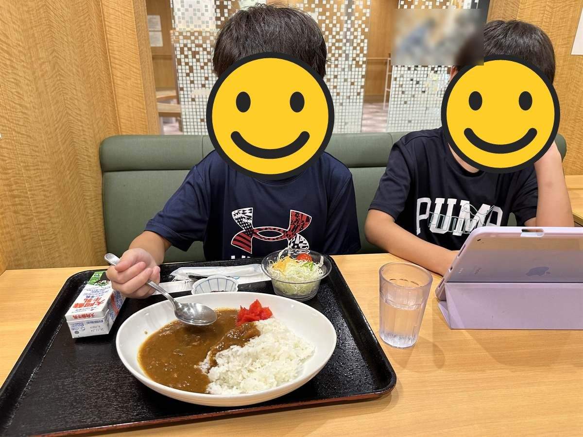 フェリーのレストランで夕食のカレーを食べる長男と、横でタブレットを見る次男