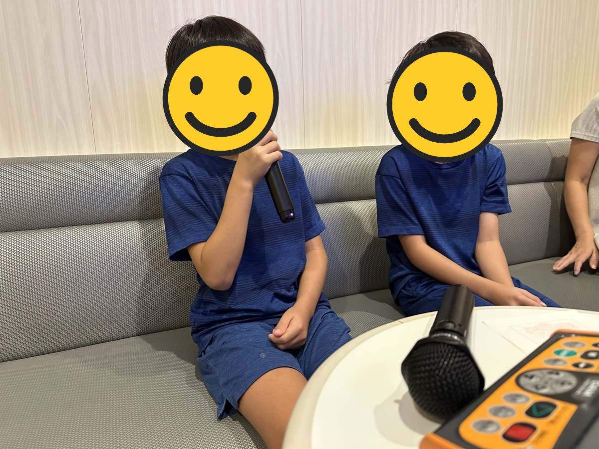フェリーのアミューズメントルームでマイクを持ってカラオケを歌う兄弟
