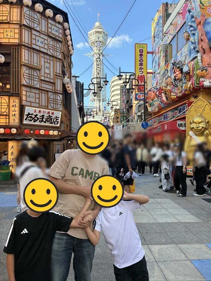 新世界の通りで、通天閣を背にパパとこども2人が並ぶ写真