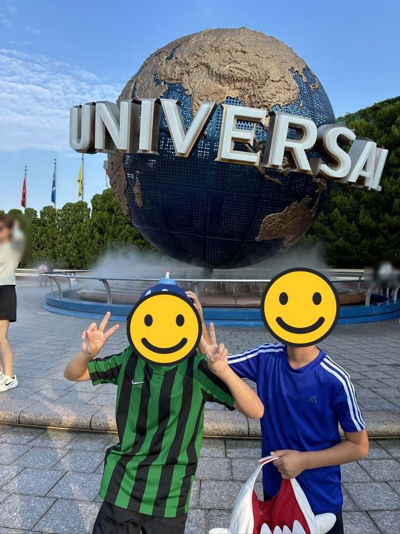 朝のUSJの地球儀の前で、ボムへいの帽子をかぶってピースする兄弟