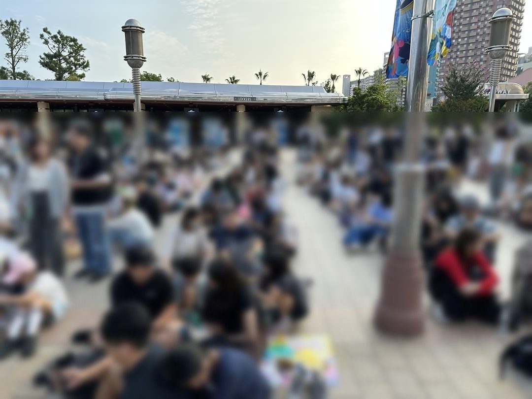 平日の朝7時、USJの入場ゲート前の広場に大勢の人が座って開園を待つ様子